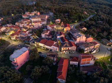 Xanthates köyü Korfu Yunanistan 'ın merkez meydanı ve kilisesinin hava manzarası, alacakaranlıkta geleneksel evler ve kiremitli çatılarla aydınlandı.