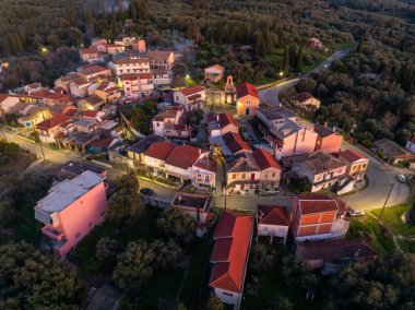 Xanthates köyü Korfu Yunanistan 'ın merkez meydanı ve kilisesinin hava manzarası, alacakaranlıkta geleneksel evler ve kiremitli çatılarla aydınlandı.