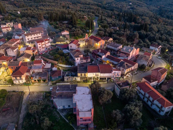 Xanthates köyü Korfu Yunanistan 'ın merkez meydanı ve kilisesinin hava manzarası, alacakaranlıkta geleneksel evler ve kiremitli çatılarla aydınlandı.