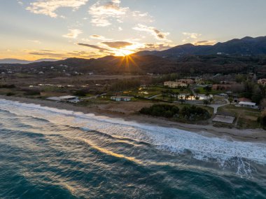 Güneş batarken Kuzey Korfu 'nun dramatik deniz manzarası sahile vuran dalgalar ve dağların yakınındaki bir tesis.