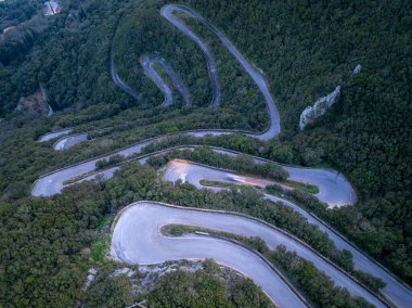 Sokraki, Korfu, Yunanistan 'da alacakaranlıkta keskin virajlı ve aydınlık patikalı aşağı sarmal dağ yolu manzarası
