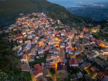 Aydınlatılmış geleneksel dağ köyü Sokraki 'nin hava panoramik manzarası uzak sahil kenti ışıkları ve İyon Denizi manzaralı, Korfu adası, Yunanistan