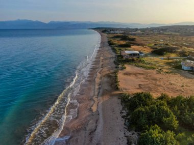 Yunanistan 'ın Kuzey Korfu kentindeki dalgalı dalgalar, altın ışık ve uzak dağlarla birlikte Acharavi sahilinin uzun kumlu kıyı şeridi üzerinde gün batımı manzarası