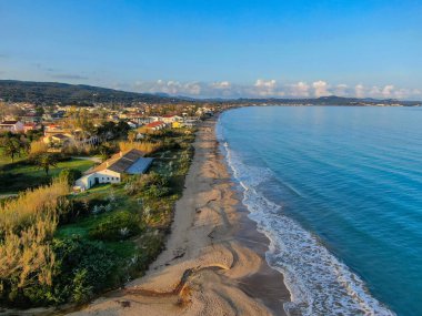 Yunanistan 'ın Kuzey Korfu kentindeki dalgalı dalgalar, altın ışık ve uzak dağlarla birlikte Acharavi sahilinin uzun kumlu kıyı şeridi üzerinde gün batımı manzarası