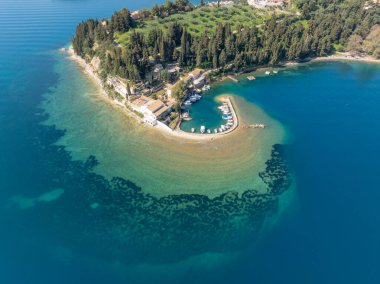 Yunanistan 'ın Korfu adasındaki turkuvaz suları, selvi ağaçları ve balıkçı tekneleri ile ikonik at nalı şeklindeki Kouloura limanının hava manzarası