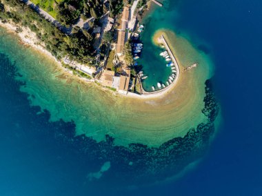 Yunanistan 'ın Korfu adasındaki turkuvaz suları, selvi ağaçları ve balıkçı tekneleri ile ikonik at nalı şeklindeki Kouloura limanının hava manzarası