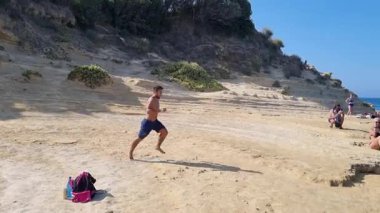 Korfu Yunanistan 'da yaz tatili sırasında Koşan ve Sarı Çamur Uçurumundan Atlayan Genç Adam Mavi Deniz suyuna