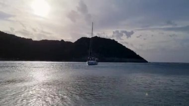 Korfu Yunanistan 'da günbatımında sakin bir deniz koyuna demirlemiş yalnız bir yelkenlinin silueti. Karanlık tepeler ve ışıldayan suyla huzurlu bir akşam atmosferi.