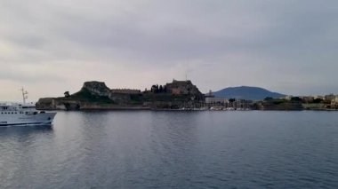 Bulutlu bir günde Yunanistan 'ın tarihi Korfu Kalesi' nden geçen beyaz yolcu feribotunun manzarası, İyon Denizi yolculuğu ve taşımacılığı