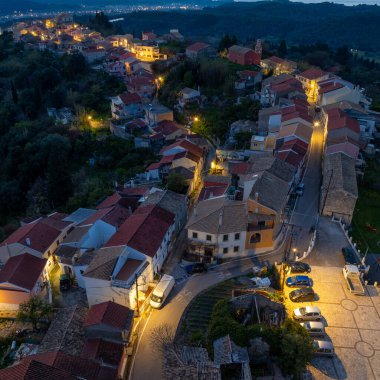 Korfu 'daki Agrafoi köyünün hava alacakaranlık manzarası aydınlanmış sokaklara ve yeşil tepelere kurulmuş geleneksel mimariye sahip Yunanistan