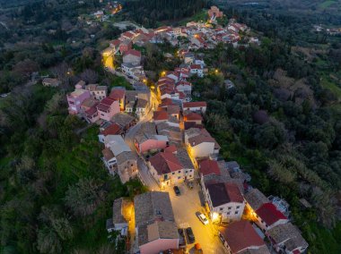 Top down aerial perspective of traditional tiled rooftops and illuminated square in Agrafoi village Corfu Greece during evening twilight