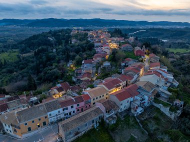 Scenic HDR aerial view of Agrafi village Corfu Greece nestled in green hills with dramatic lighting on traditional houses and red roofs during a beautiful sunset over the Ionian landscape