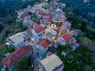Yunanistan 'ın Corfu Adası' ndaki geleneksel Antipernoi köyünün akşamüstü alacakaranlığı sırasında aydınlık sokakları ve kırmızı kiremitli çatıları olan hava manzarası.