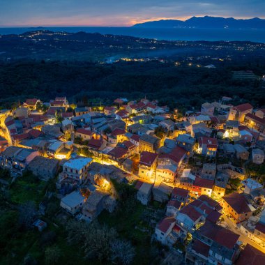 Yunanistan 'ın Korfu kentindeki ünlü seyahat noktası günbatımı parıltısıyla mavi saatte doğaya yuva yapmış Nymfes köyünün insansız hava aracı görüntüleri.