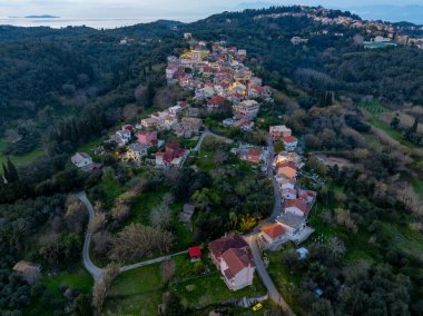Yunanistan 'ın Kuzey Korfu kentindeki Antiperni köyünün hava manzarasında geleneksel kırmızı çatılı evler, yeşil tepeler ve uzak deniz manzarası yer alıyor.