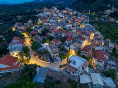 Yunanistan 'ın Korfu adasındaki dağlarda geleneksel mimari ve dolambaçlı yolların yer aldığı, aydınlanmış Nimfes köyünün alacakaranlıktaki hava manzarası