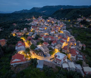 Yunanistan 'ın Korfu adasındaki dağlarda geleneksel mimari ve dolambaçlı yolların yer aldığı, aydınlanmış Nimfes köyünün alacakaranlıktaki hava manzarası