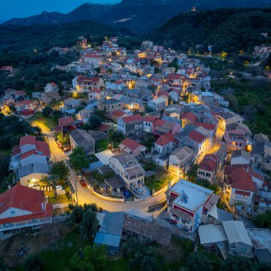 Yunanistan 'ın Korfu adasındaki dağlarda geleneksel mimari ve dolambaçlı yolların yer aldığı, aydınlanmış Nimfes köyünün alacakaranlıktaki hava manzarası