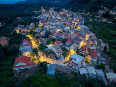 Yunanistan 'ın Korfu adasındaki dağlarda geleneksel mimari ve dolambaçlı yolların yer aldığı, aydınlanmış Nimfes köyünün alacakaranlıktaki hava manzarası