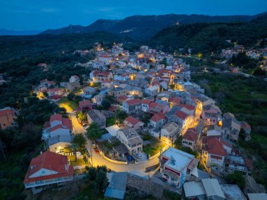 Yunanistan 'ın Korfu adasındaki dağlarda geleneksel mimari ve dolambaçlı yolların yer aldığı, aydınlanmış Nimfes köyünün alacakaranlıktaki hava manzarası