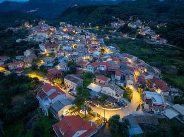 Yunanistan 'ın Korfu adasındaki dağlarda geleneksel mimari ve dolambaçlı yolların yer aldığı, aydınlanmış Nimfes köyünün alacakaranlıktaki hava manzarası
