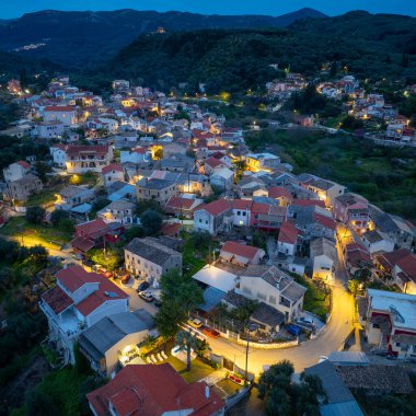 Yunanistan 'ın Korfu adasındaki dağlarda geleneksel mimari ve dolambaçlı yolların yer aldığı, aydınlanmış Nimfes köyünün alacakaranlıktaki hava manzarası