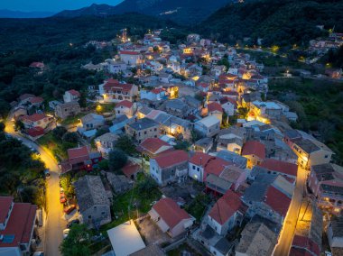Drone photography of Nymfes Corfu with red roof houses and church amidst green nature and mountains in the Ionian sea region