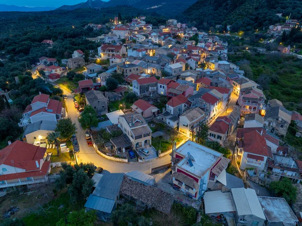 Yunanistan 'ın Korfu adasındaki dağlarda geleneksel mimari ve dolambaçlı yolların yer aldığı, aydınlanmış Nimfes köyünün alacakaranlıktaki hava manzarası