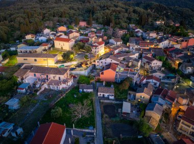 Korfu adasındaki Valanio köyünün hava aracı manzarası alacakaranlıkta aydınlatılmış sokaklar ve yeşil dağlara kurulmuş geleneksel evlerle Yunanistan