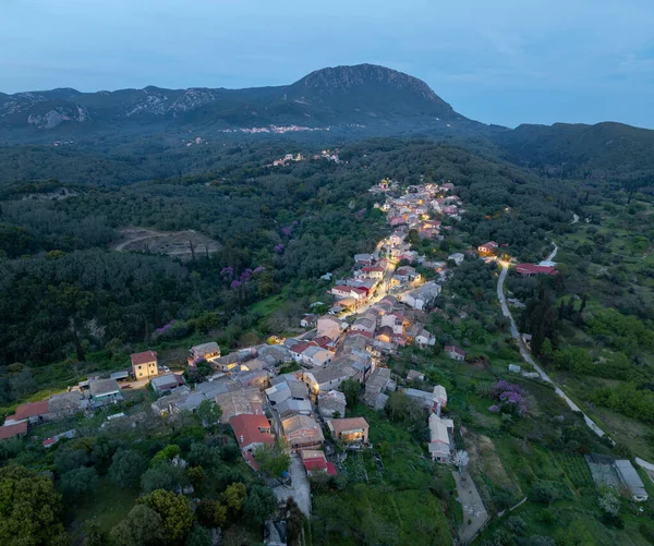 Korfu 'daki Zigos köyünün panoramik hava aracı görüntüsü alacakaranlıkta geleneksel evleri ve engin yeşil dağ manzarasını barındırıyor