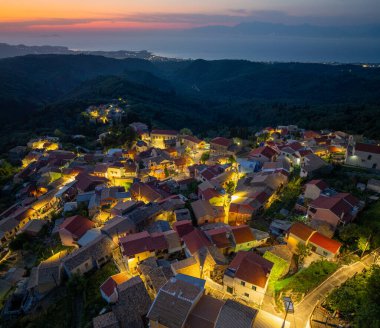 Günbatımında Episkepsi köyünün panoramik hava aracı görüntüleri dramatik gökyüzü, aydınlık sokaklar ve Yunanistan 'ın Korfu adasındaki uzak kıyı şeridi