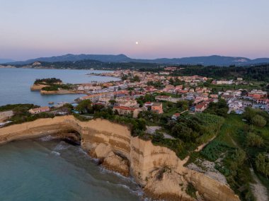Sidari kıyılarının kumtaşı uçurumları ve Kuzey Korfu Yunanistan 'daki köy üzerinde yükselen dolunaylı panoramik manzarası alacakaranlık sırasında