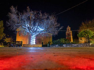 Agioi Douloi köy meydanındaki ışıklandırılmış ağaç ve kilise çan kulesi Noel boyunca Noel süslemeleri ile Korfu Yunanistan 'da gece yarısı