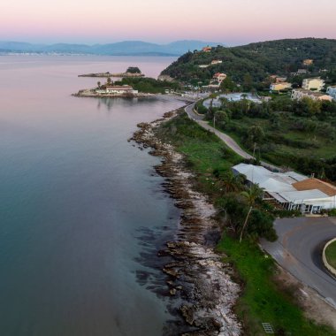 Huzurlu deniz manzarası Agios Spiridon Corfu Yunanistan 'daki kayalık sahillerin kıvrımlarını gösteriyor. Pembe bir günbatımı gökyüzü ve durgun İyon Denizi