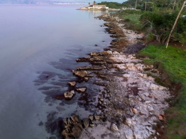 : Korfu Yunanistan 'ın Agios Spiridon kıyısı boyunca akşam erken saatlerde sivri kayalardan ve temiz sığ sudan oluşan alçak irtifa drone görüntüsü