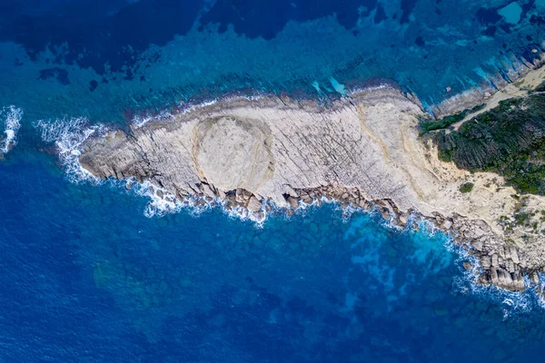 Agios Stefanos 'un burnu, Korfu, Yunanistan' da beyaz köpük ve doku oluşturan kayalık kayalık kıyılara çarpan dalgaların yukarıdan aşağıya doğru görüntüsü