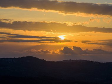 Güneşin yatay bulut katmanlarının arasından süzülerek Akdeniz 'deki karanlık bir tepe manzarasına ışınlar saçtığı manzaralı bir gün batımı.
