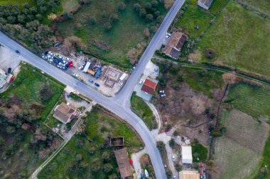 Hava kuşları, Corfu kırsalında inşaat halindeki bir evin ve çeşitli araçların kesiştiği kırsal bir yola bakıyor.