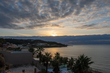 Tropikal deniz üzerinde güzel bir gün batımı, Agios Stefanos, Corfu, Yunanistan 'daki kıyı köyü manzarası: canlı gökyüzü, renkli bulutlar, ve palmiye ağaçları ile altın saat okyanus yansıması.
