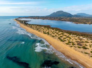 Halikounas Sahili ve Korission Gölü üzerindeki geniş hava aracı manzarası yeşil dağlara, nefes kesen kıyı manzarasına ve Yunanistan 'ın Korfu adasındaki kumlu kumullara bakıyor