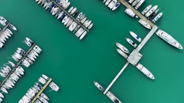 Gouvia Marina Corfu Yunanistan 'daki rıhtımlarda simetrik olarak dizilmiş, zümrüt yeşili liman suyu ve denizcilik gemilerinin dikey görüntüsü.