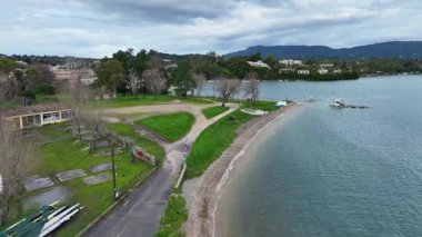 Bulutlu bir günde Gouvia, Corfu, Yunanistan 'daki Yeşil Sahil Kıyısı ve Sakin Kıyı Sularının Havadan Görünümü, Bereketli Bitkiler, Bir Paved Yolu ve Manzaralı Deniz Manzarası