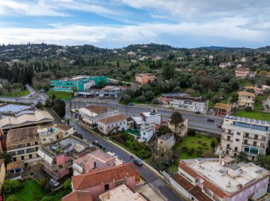 Yunanistan 'ın Korfu adasındaki Gouvia kentinin panoramik şehir manzarası konut binaları, yollar, yeşil tepeler, selvi ağaçları ve Diellas süpermarketlerini gösteriyor
