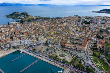 Korfu şehrinin yüksek açılı insansız hava aracı görüntüleri ticari limanı, Eski Liman 'ı, tarihi binaları ve bulutlu gökyüzünün altındaki Paleo Frourio kalesini gösteriyor, Kerkyra Adası.