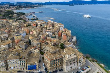 Korfu Eski Kasabası 'nın yoğun terracotta çatıları üzerinde yüksek açılı hava manzarası ve arka planda feribot var. Kerkyra 'nın tarihi merkezinde geleneksel Venedik tarzı mimari ve renkli binalar