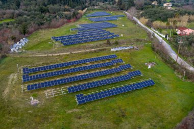 Yunanistan 'da, bulutlu bir gökyüzü altında yere monte edilmiş bir güneş dizisinin havadan görünüşü, tek kristalli paneller ile gündüz hafif dağınık ışıklandırmayla donatılmış fotovoltaik kurulum