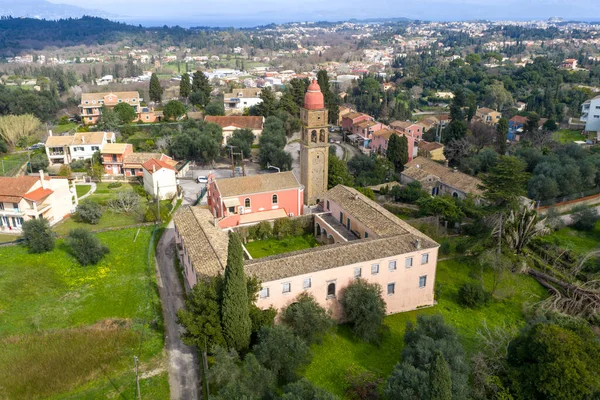 Korfu, Kompitsi 'deki tarihi Agioi Apostoloi Kilisesi. İkonik Venedik tarzı kırmızı çan kulesi ve geleneksel Yunan Ortodoks mimarisinin yer aldığı hava çekimi bir köy ortamında
