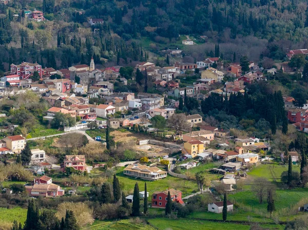 Yunanistan 'ın Korfu adasındaki yoğun yeşillikler arasında renkli evleri ve kilise çan kulesi olan geleneksel bir dağ köyünün telefoto görüntüsü.