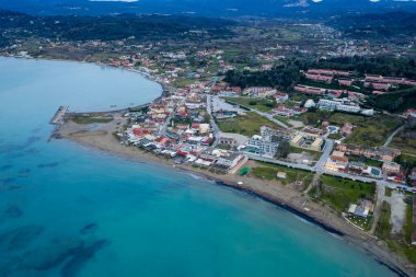 Yunanistan 'ın Kuzey Korfu kentindeki Sidari sahil beldesi ve kumlu plajın insansız hava aracı görüntüsünde, alacakaranlıkta turkuaz su ve oteller bulunan panoramik İyon deniz manzarası yer alıyor..