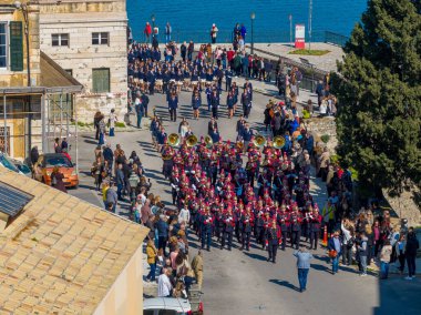 Korfu kasabası Greec 'in kıyı caddeleri boyunca Ortodoksluk Pazar günü Aziz Theodora' nın kutsal emanetinin dini törenini kutlayan kırmızı üniformalı bando bandosunun yüksek açılı görüntüsü.